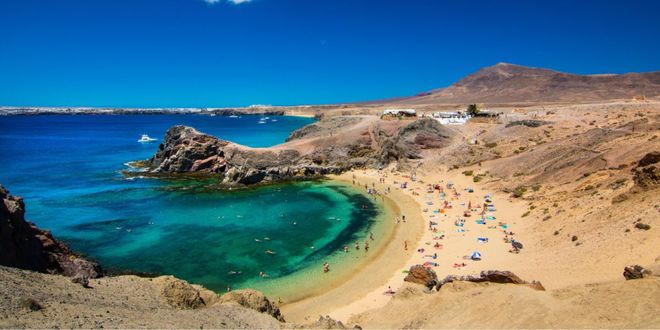 Veraneantes disfrutando de la playa del Papagayo, de arena dorada y aguas turquesas, en Lanzarote