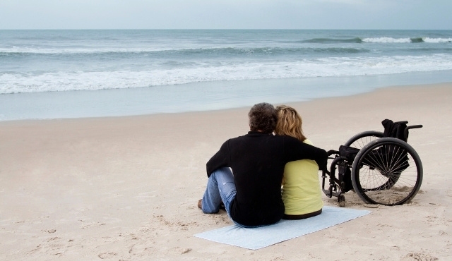 Pareja en una playa de España y una silla de ruedas