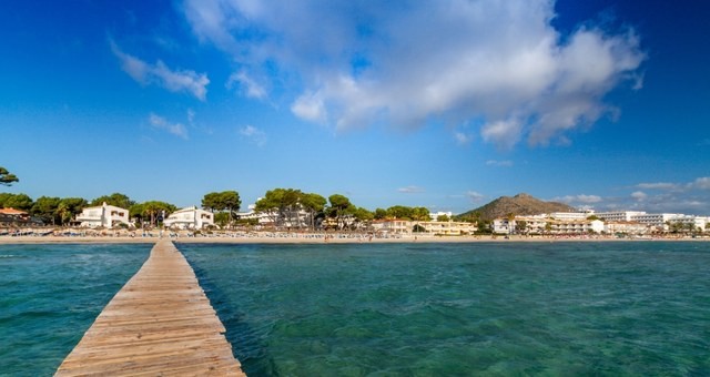 Beach with trees and a wooden pier in Alcúdia, Mallorca