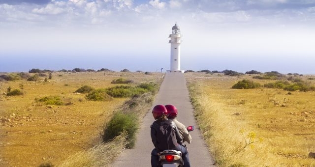 Couple on a scooter riding to Cap de Barbaria lighthouse in Formentera, Spain