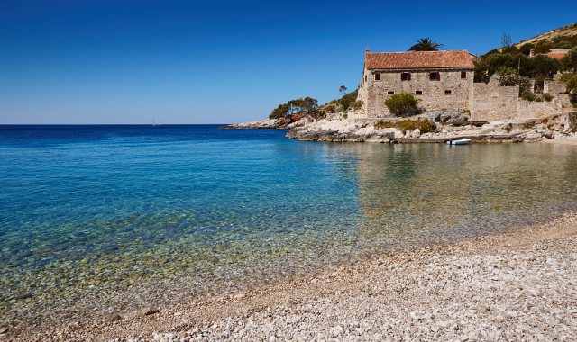 Der lange Strand Dubovica mit weißen Kieselsteinen und alten Steinhäusern