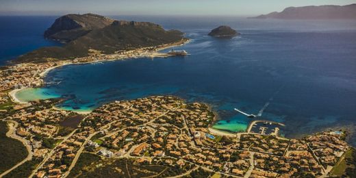 An aerial view of Golfo Aranci, in Sardinia, Italy, featuring a bay with a ferry moored at its port