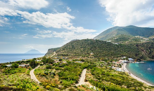 Panoramic view of Filicudi in the Aeolian Islands, with a road winding through green hills and a beach in the distance