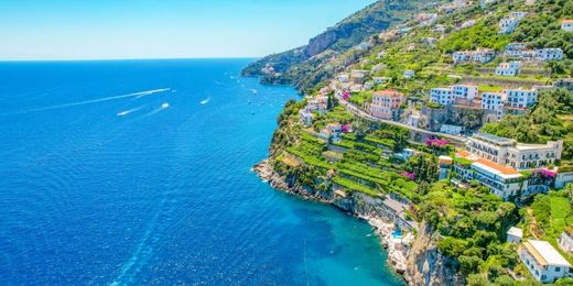 Vista della Costiera Amalfitana con edifici arroccati sui pendii verdeggianti e barche nel mare