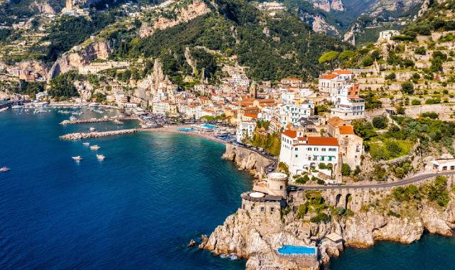 Vista aerea di Amalfi con case e edifici arroccati lungo la costa di fronte al porto e al mare blu