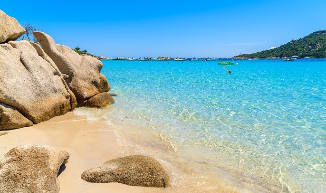  Rocce sulla spiaggia di Santa Giulia, in Corsica, con il mare cristallino e delle barche in lontananza