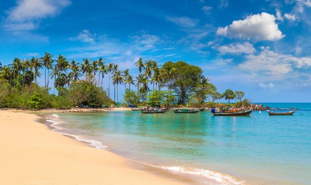 Golden sandy beach in Koh Lanta, Thailand, with palm trees and small boats at sea