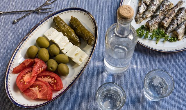 Table with bottle of ouzo, glasses and plates with sardines, olives, feta cheese and dolma