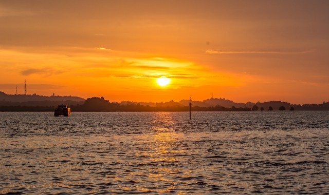Orange skies as sun sets over Batam, Indonesia, with ferry at sea in the distance