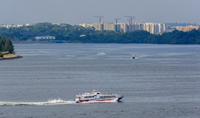 Fast ferry at sea crossing the Strait on Singapore with tall buildings and trees in the distance