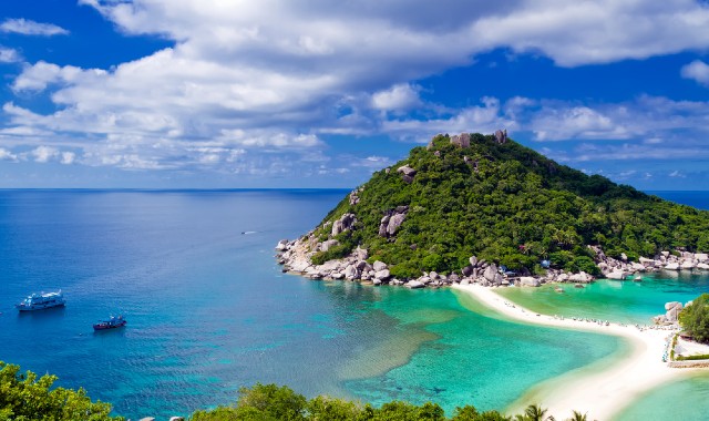 Ferries sailing near the shores of Ko Pha-ngan, where a narrow strip of beach is surrounded by green hills