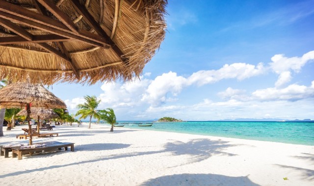 A sunny, white beach in Koh Lipe, Thailand, with tall palm trees, sunbeds, and parasols