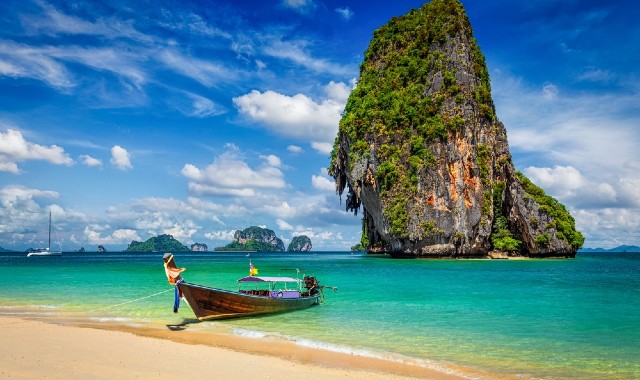 A traditional long-tail boat pulled up on a tropical beach with limestone rocks in background in Krabi, Thailand