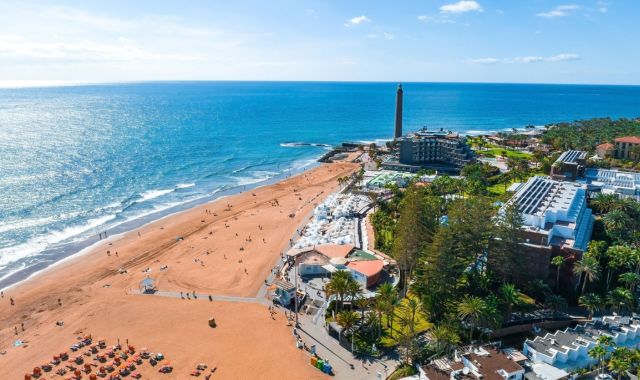 Vista panoramica della spiaggia di Meloneras, con file di lettini, edifici e il faro di Maspalomas in lontananza