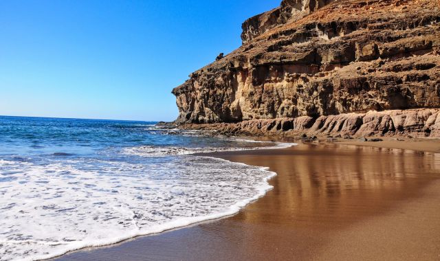 Onde in arrivo sulla riva di una spiaggia a Gran Canaria, con delle scogliere rocciose a fare da sfondo
