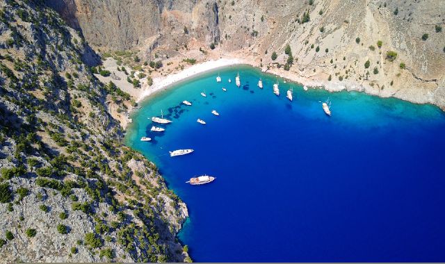 Small boats anchored in the blue waters of Agios Georgios Beach, with imposing cliffs all around