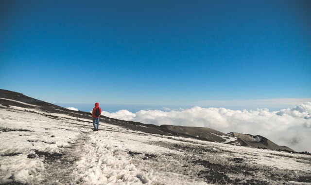 Una persona in un cappotto rosso che osserva il panorama innevato dell'Etna