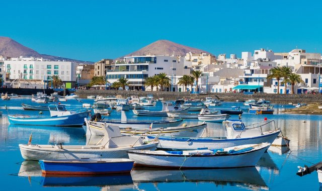 Small boats moored along the docks of Arrecife, in Lanzarote, with white buildings and mountains in the background