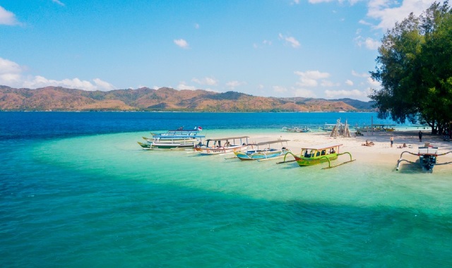 Small boats moored on a beach in Lombok, with white sand and mountains in the background