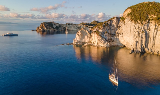 Barche che navigano nel mare blu vicino alla costa rocciosa di Ponza al tramonto