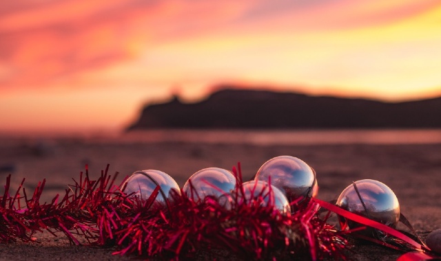 Addobbi natalizi posizionati su una spiaggia sarda in primo piano e il tramonto sul mare in lontananza