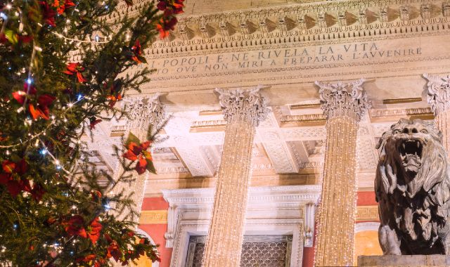 Le colonne del Teatro Massimo di Palermo ricoperte di luci natalizie che brillano tra un albero di Natale e una statua leonina