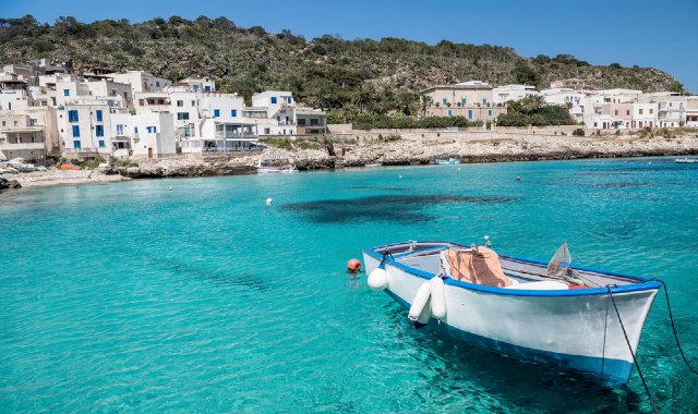 Una barca da pesca vicino alla riva di Levanzo, con casette bianche lungo la costa