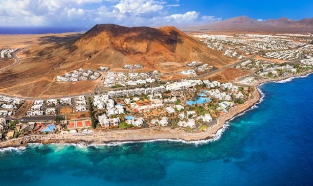 Vista aerea di Playa Blanca, a Lanzarote, con le sue case bianche e un vulcano dai pendii rossi che si affaccia sul mare