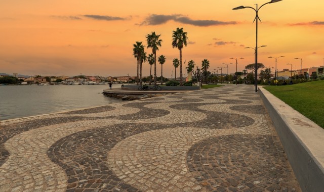 Tramonto sul lungomare di Olbia, tra palme e una passeggiata pedonale a ciottoli