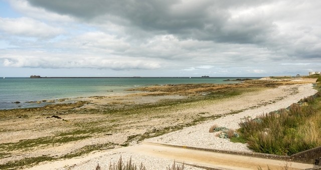 Long strip of beach with white sand and vegetation along the coast of Cherbourg in France