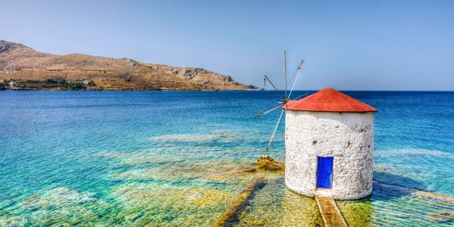 A white stone windmill with a red roof standing in the clear turquoise sea of Leros, Greece