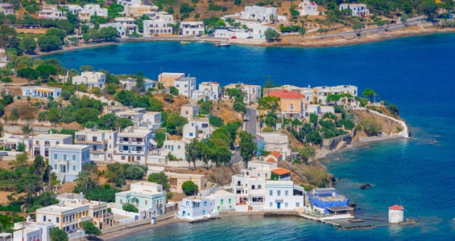 Panoramic view of Agia Marina village with white houses, green trees, and blue bay in Leros, Greece