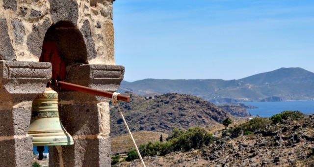 Close-up of a stone bell tower overlooking the arid hills and blue sea of Patmos, Greece