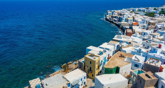 Aerial view of white and yellow houses of Mandraki village along the deep blue coast of Nisyros, Greece