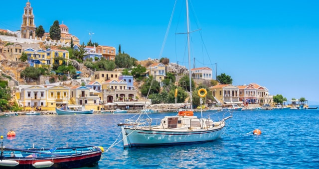Colorful neoclassical houses and a bell tower overlooking sailboats in Gialos harbor in Symi, Greece