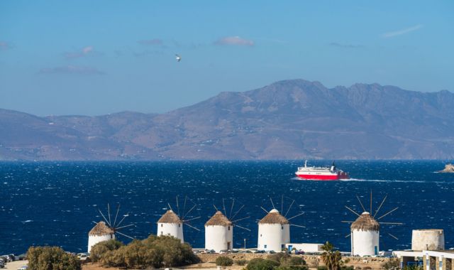 View of ferry passing by windmills in Mykonos, Cyclades, Greece