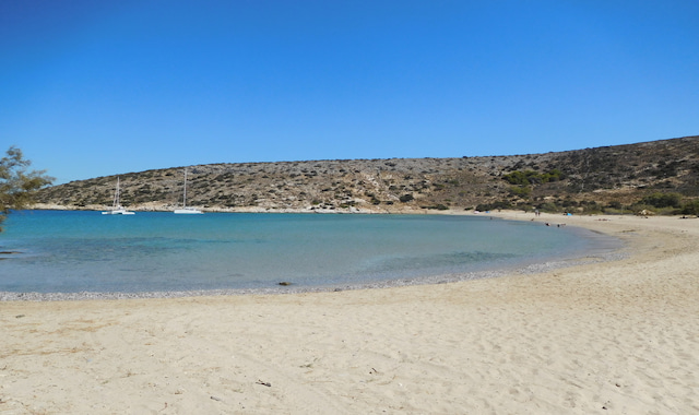A wide sandy shore and calm blue waters at Livadi Beach with sailboats on Iraklia island in Greece