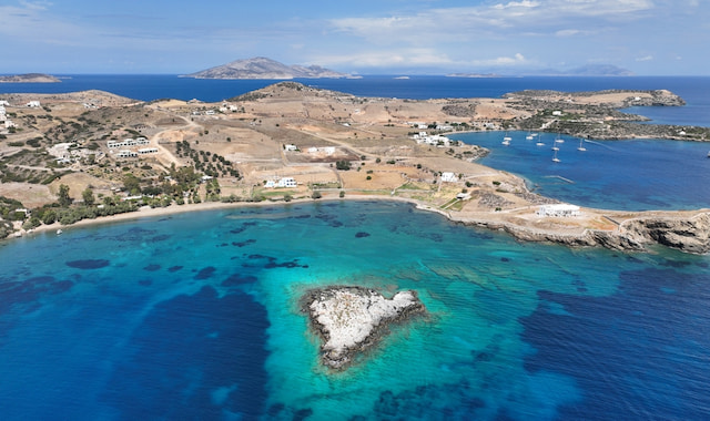 Aerial panoramic view of the blue coastline, islets, and countryside surrounding Tsigouri Beach in Schinoussa, Greece