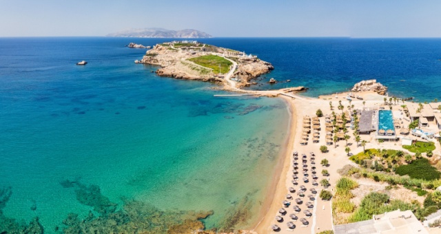 Koumbara beach with sun loungers and a rocky peninsula in Ios, Greece