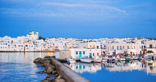 White buildings and fishing boats reflected in the calm water of Naoussa port at twilight in Paros, Greece