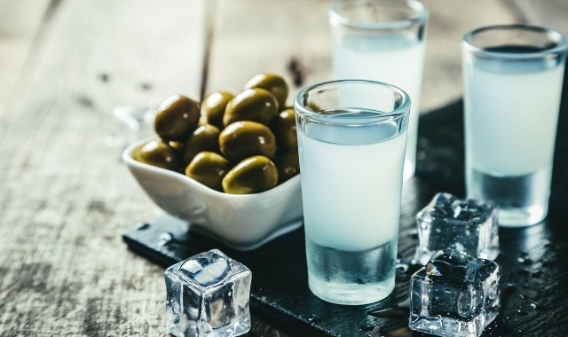 Glasses with traditional aperitif ouzo served with green olives on the side and decorated with ice cubes