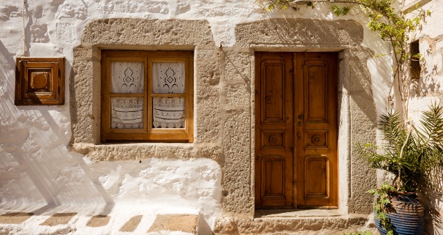 Tradycyjny dom w Chorze na Patmos z drewnianymi drzwiami i haftowanymi zasłonkami