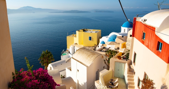 view from Santorini, white houses, blue, orange and yellow details, purple flower, ferry routes to santorini 2020