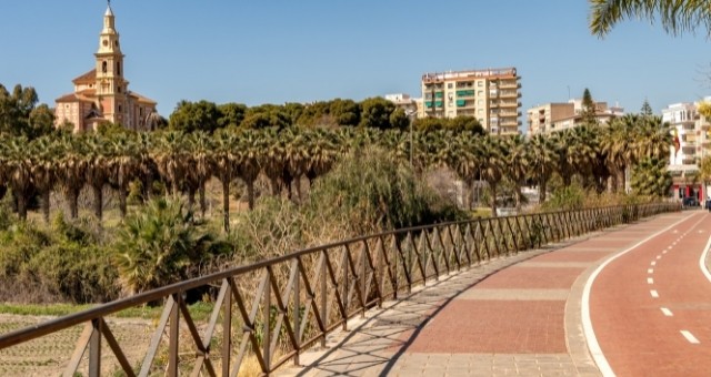 A bike path lined with palm trees and buildings in Pueblos de América Park, Motril, Spain