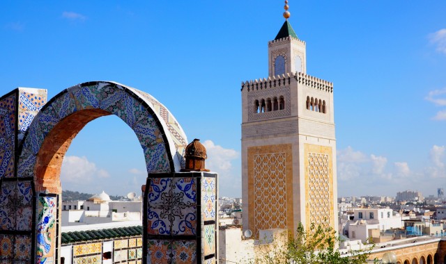  Le minaret de la mosquée El-Zitouna vu à travers des arches de tuiles colorées depuis un toit à Tunis